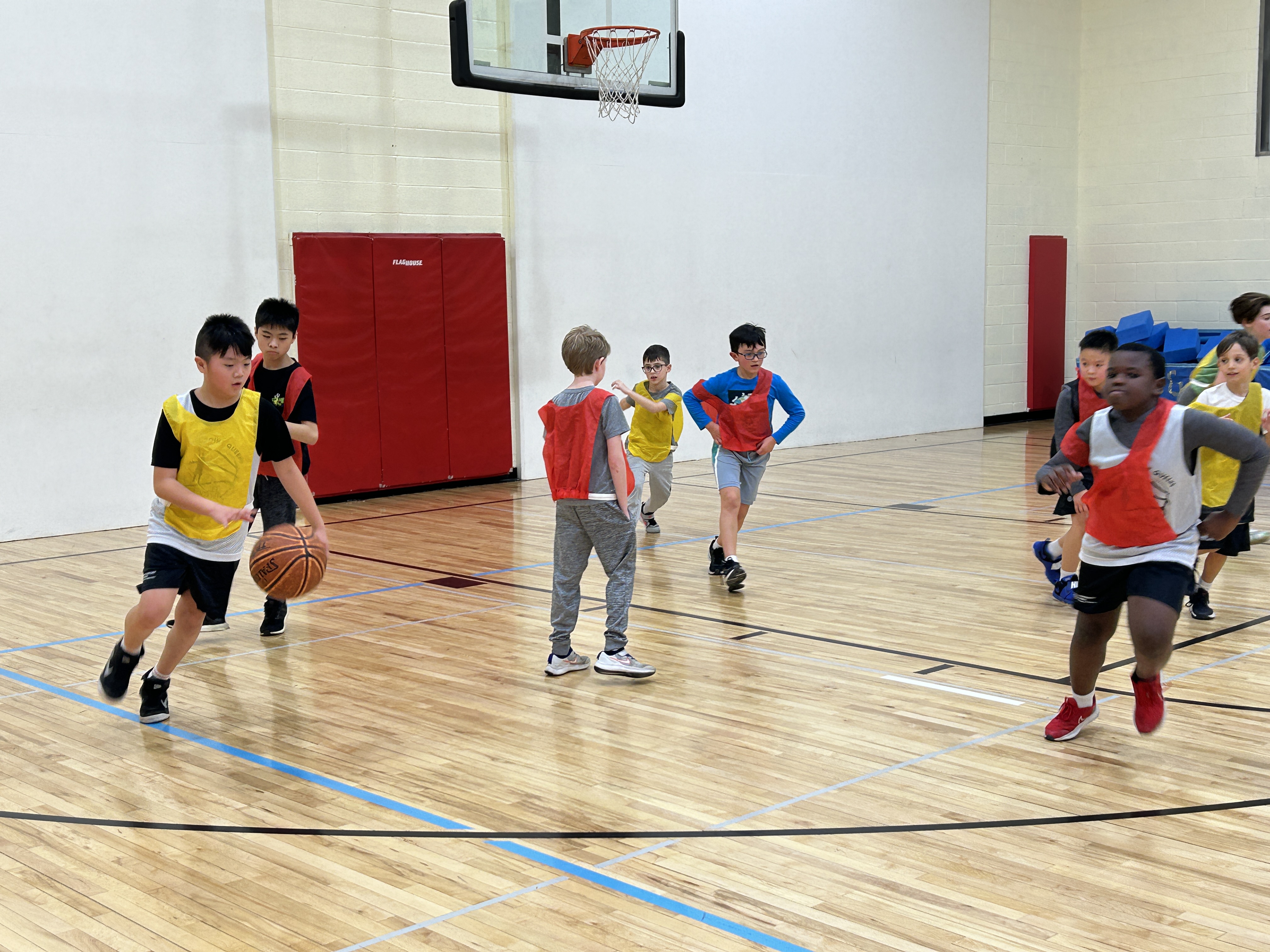 A group of kids playing basketball in a gym located in Little Neck.
