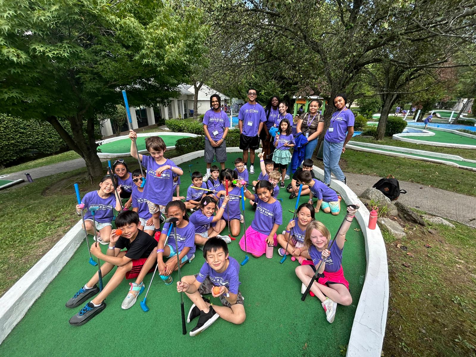 A group of children posing for a photo at a mini golf course during summer camp.