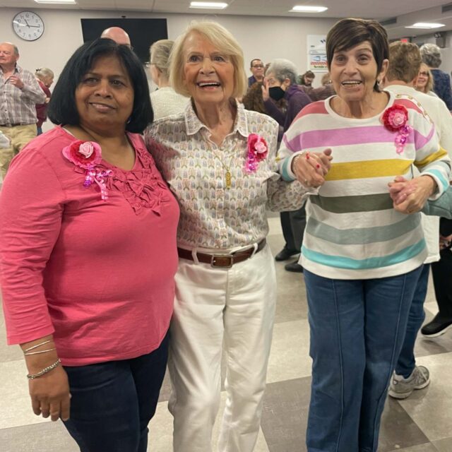 A group of women standing in a room with pink ribbons.