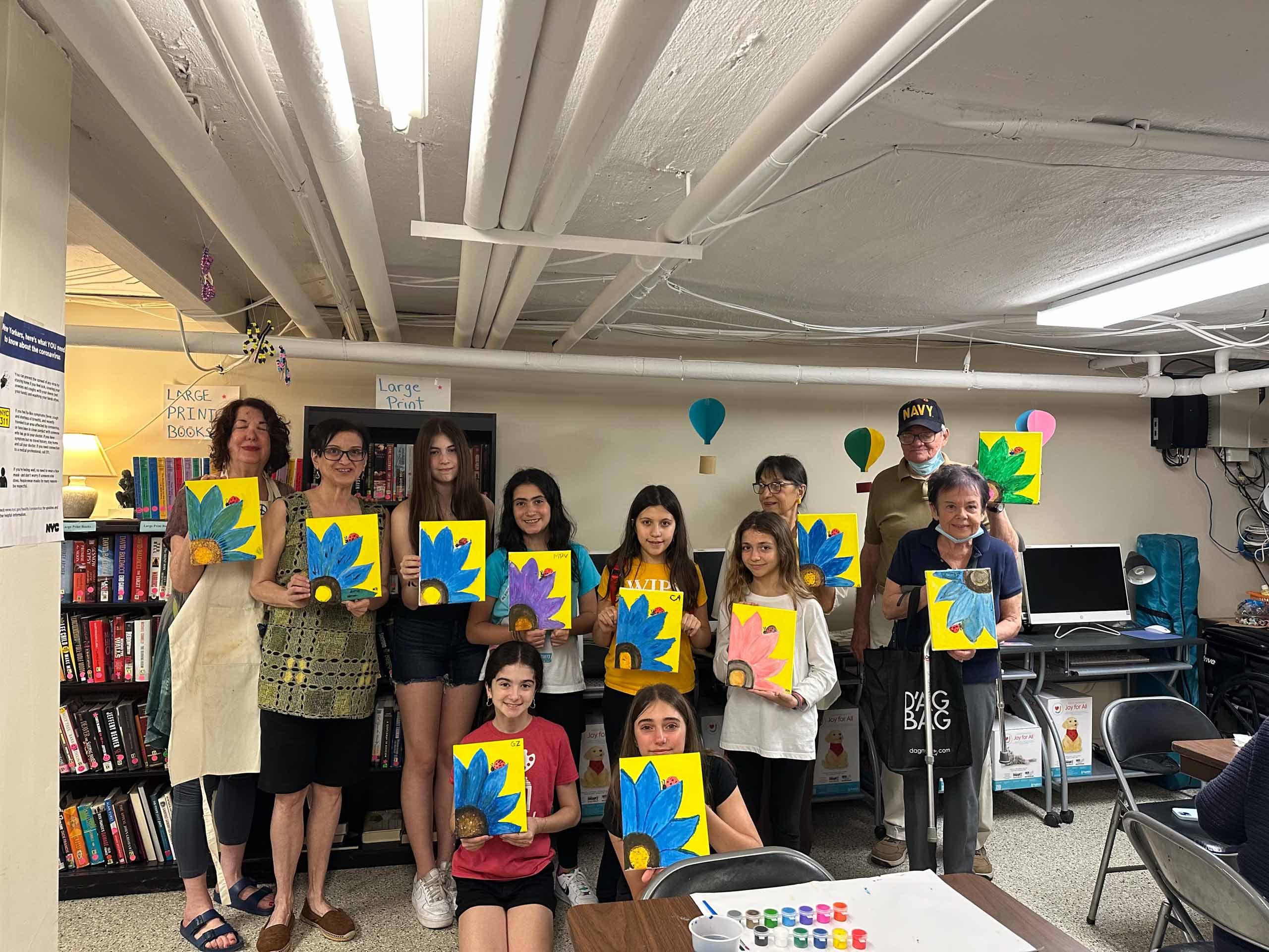 A group of people holding up colorful paintings in a room.