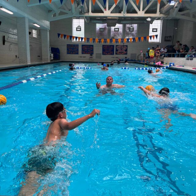 A group of people playing water polo in an indoor pool.