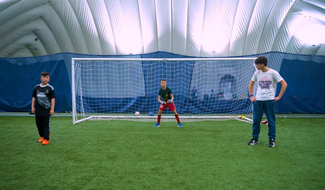 A group of kids standing in front of a goal in an indoor soccer field.