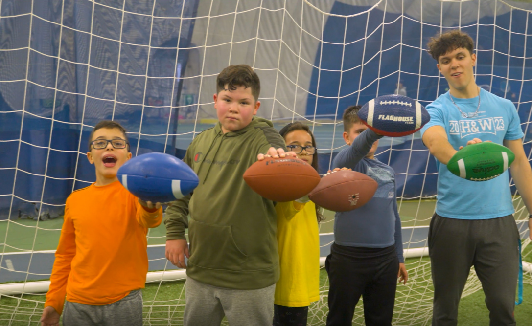 A group of kids holding footballs in front of a goal.