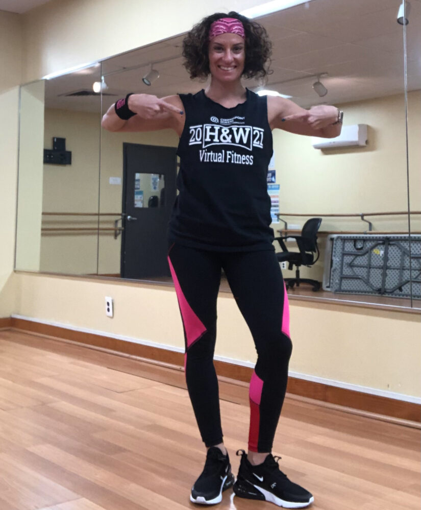 A woman in a black tank top and pink leggings posing in a dance studio.