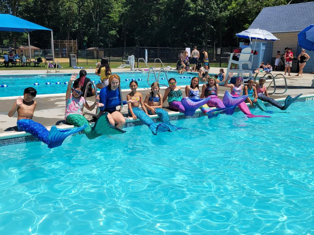 A group of children in mermaid tails sitting on the edge of a pool.