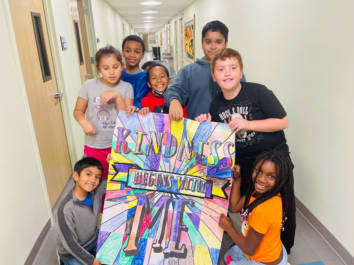 A group of kids posing with a sign in a hallway.