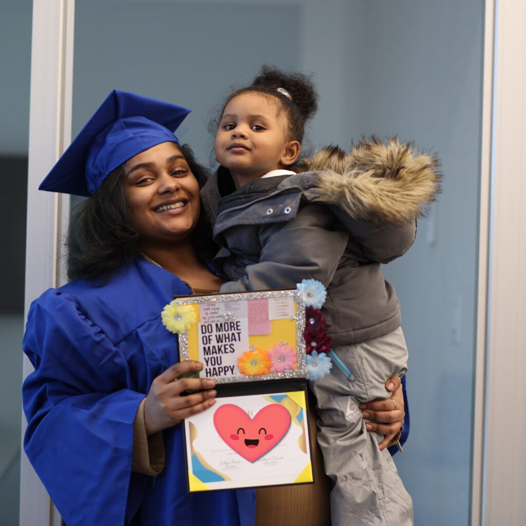 A woman in a graduation gown holding a child.