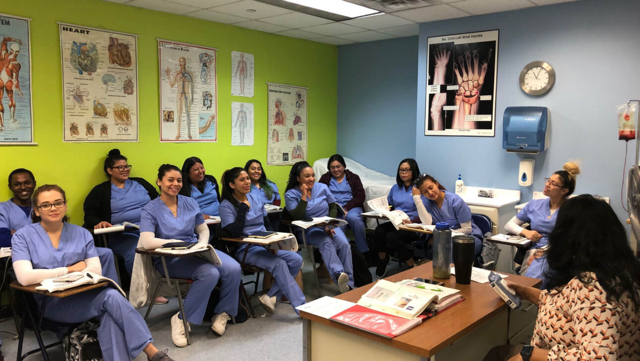 A group of women in scrubs sitting in a classroom.