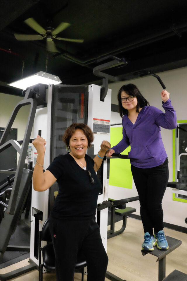 Two women standing on a gym machine.