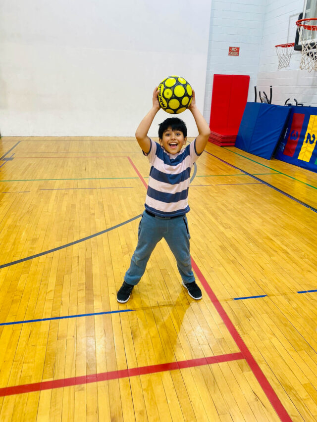 A young boy holding a soccer ball in a gym.