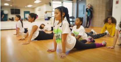 A group of young girls practicing yoga in a dance studio.