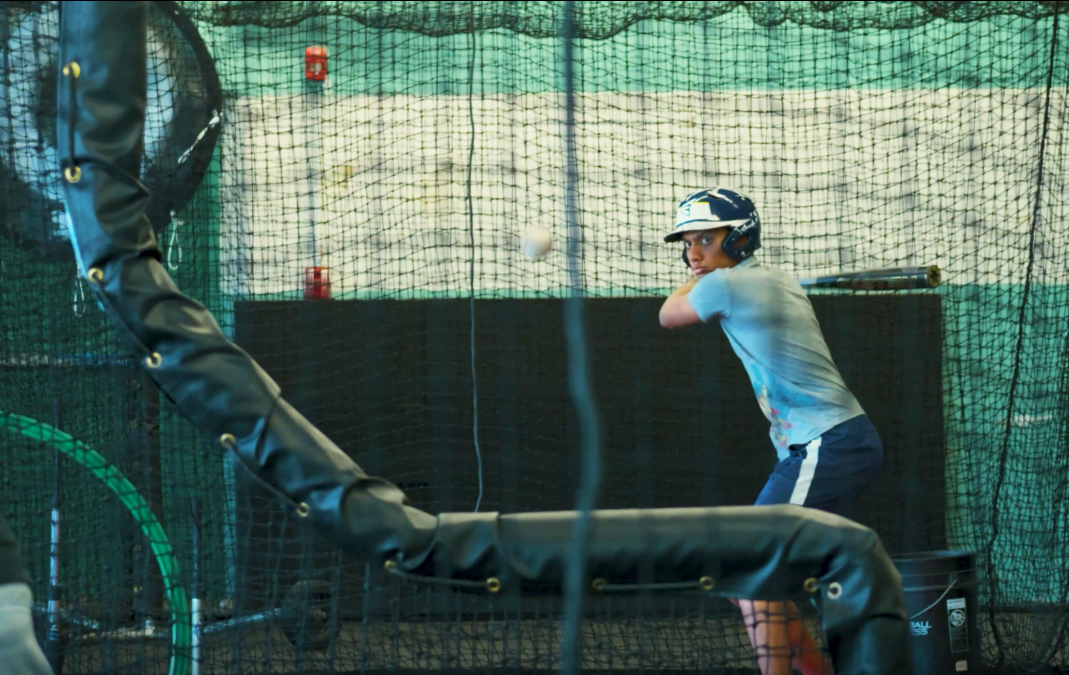 A baseball player swinging at a ball in a batting cage.