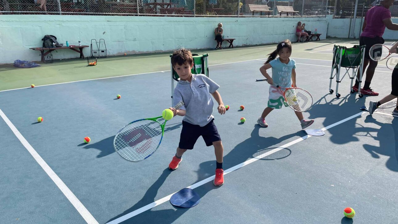 A group of children playing tennis on a court.
