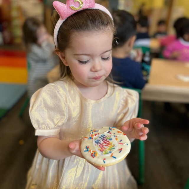 A little girl holding a cookie in front of a table.