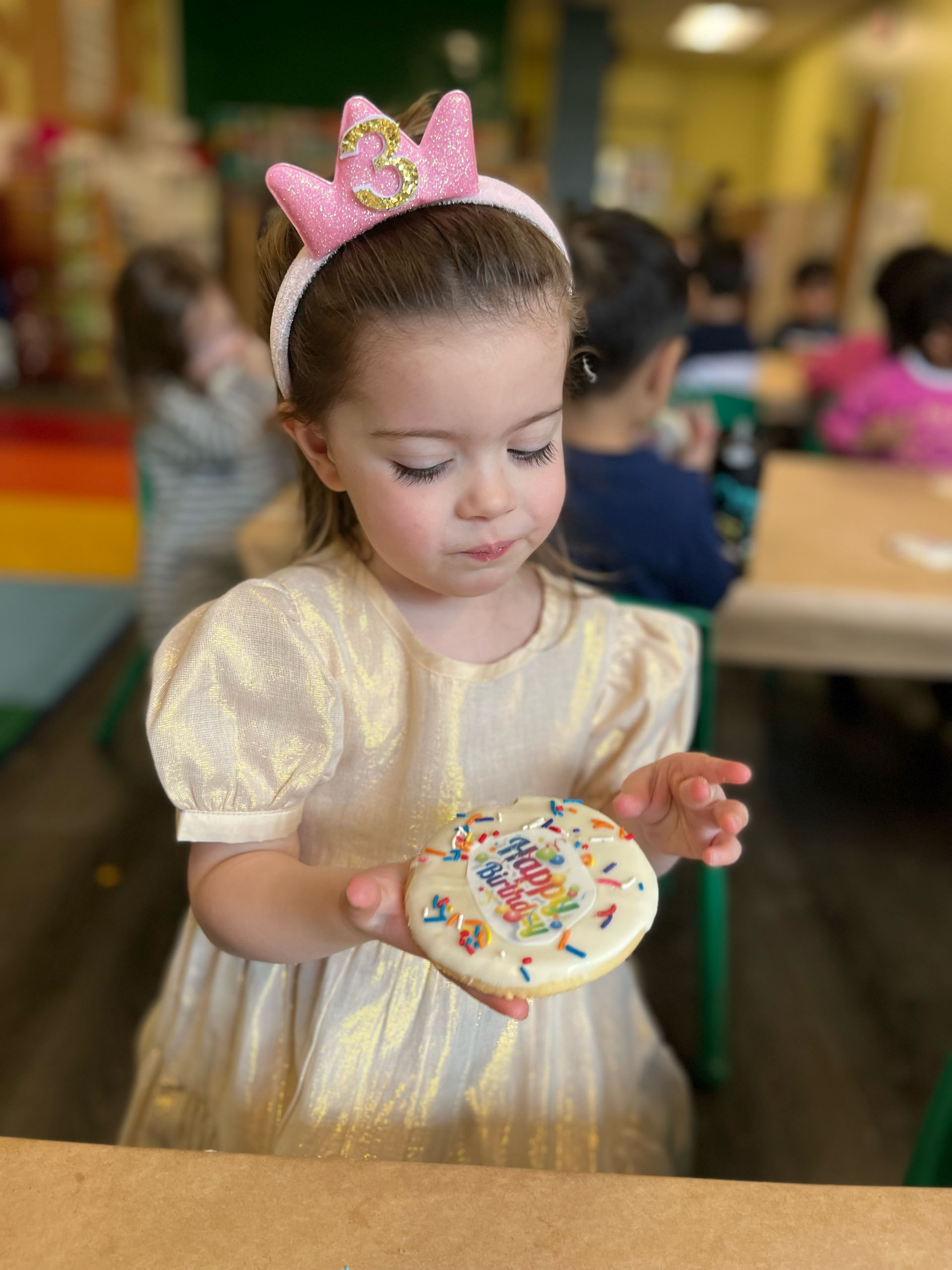 A little girl holding a cookie in front of a table.