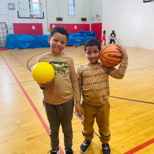 Two boys holding basketballs in a gym.
