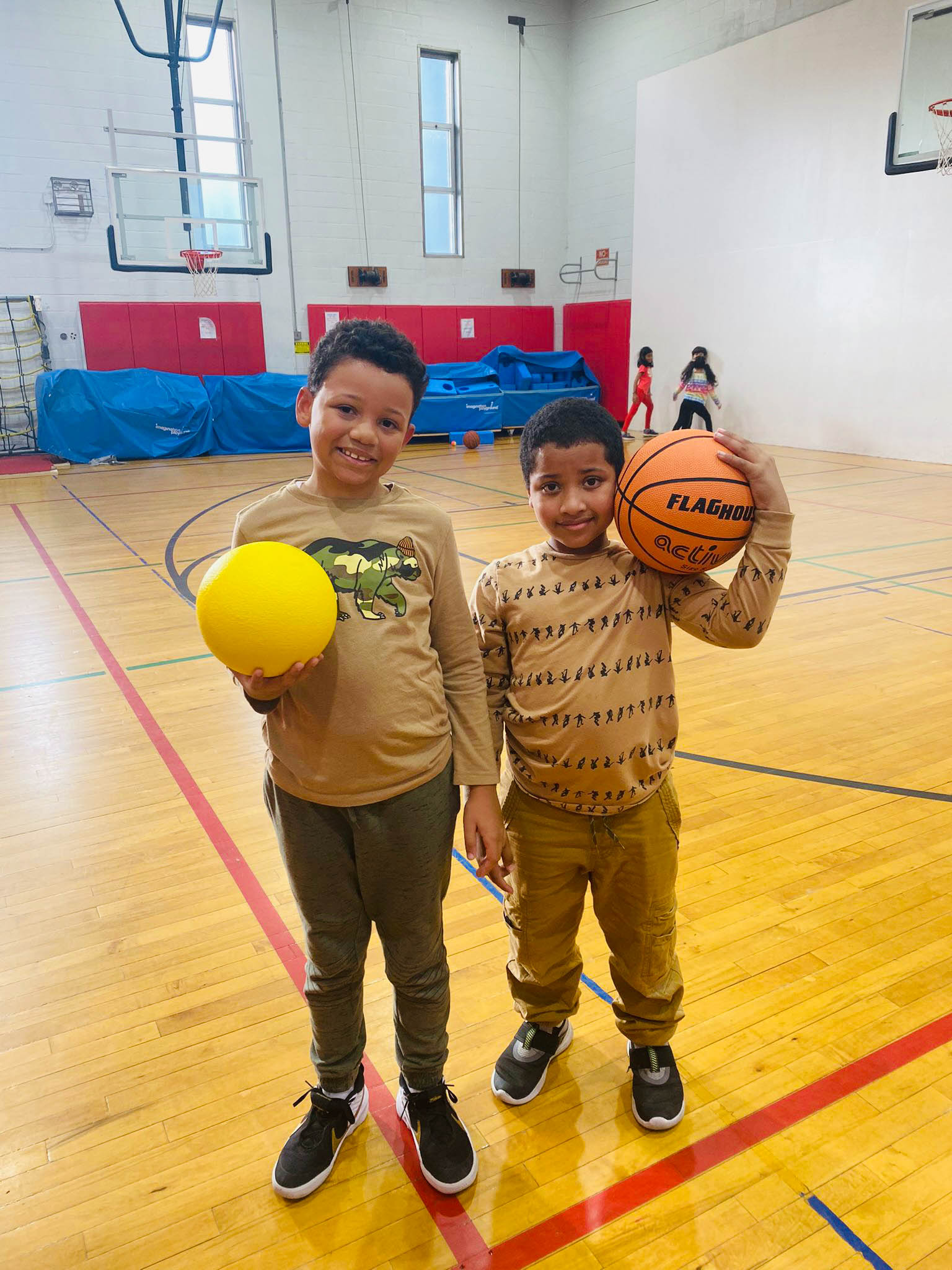 Two boys holding basketballs in a gym.
