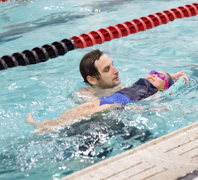 A man with a child in a swimming pool at a summer camp.