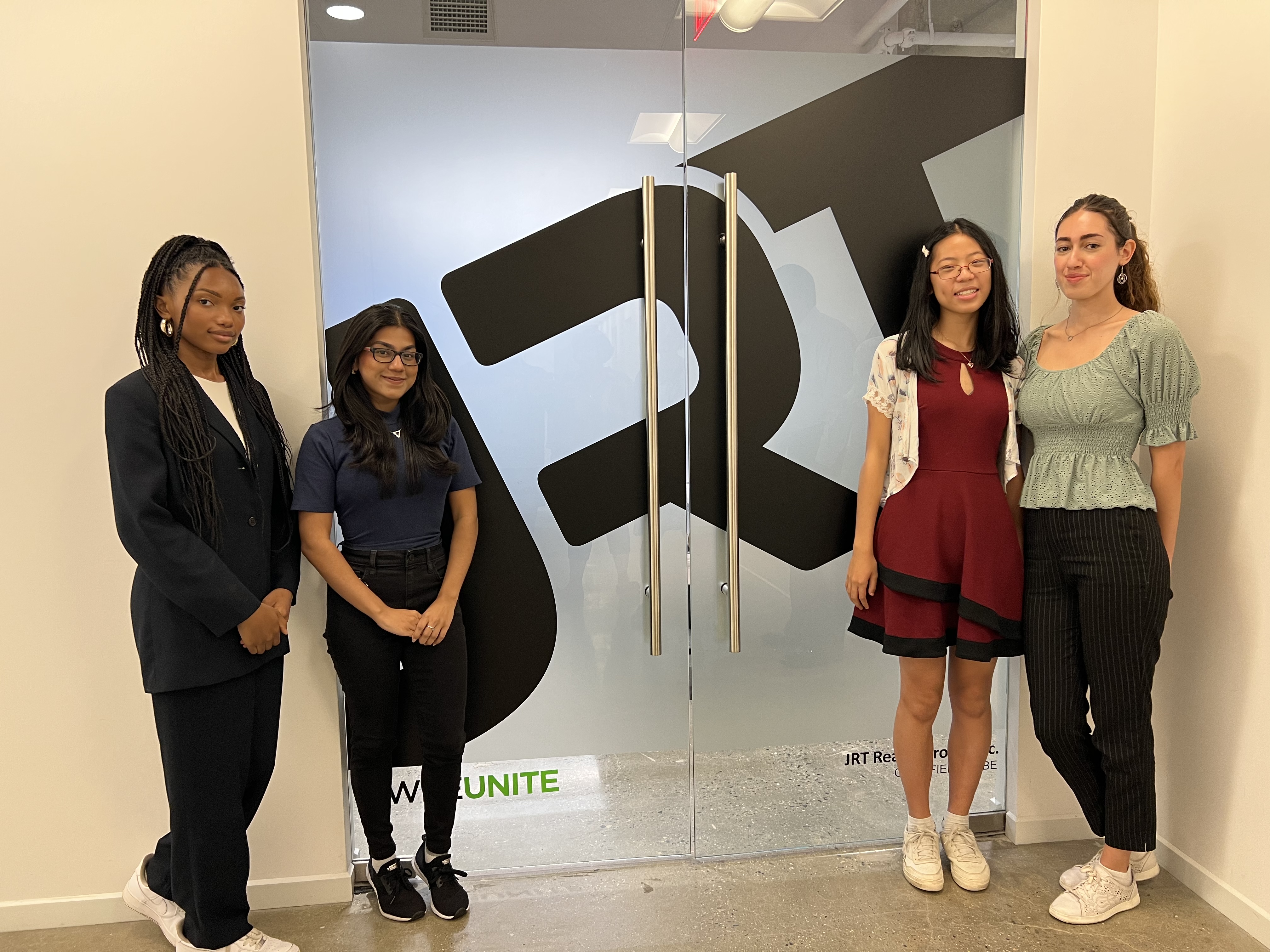 Four young women standing in front of a glass door, showcasing their auto drafting skills.