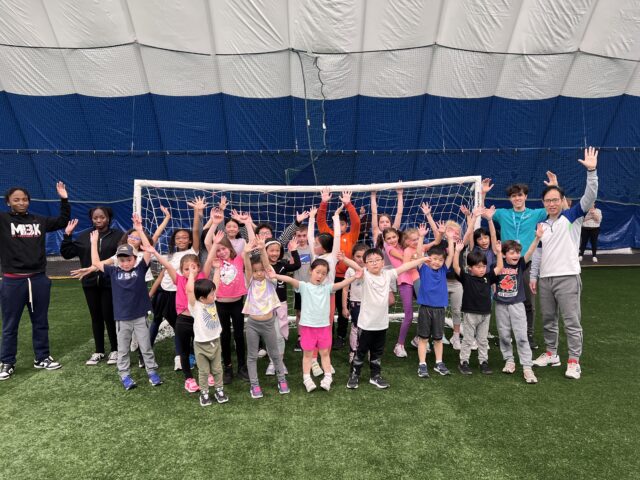 A group of children participating in mini camps, standing in front of a soccer goal during the end of summer.