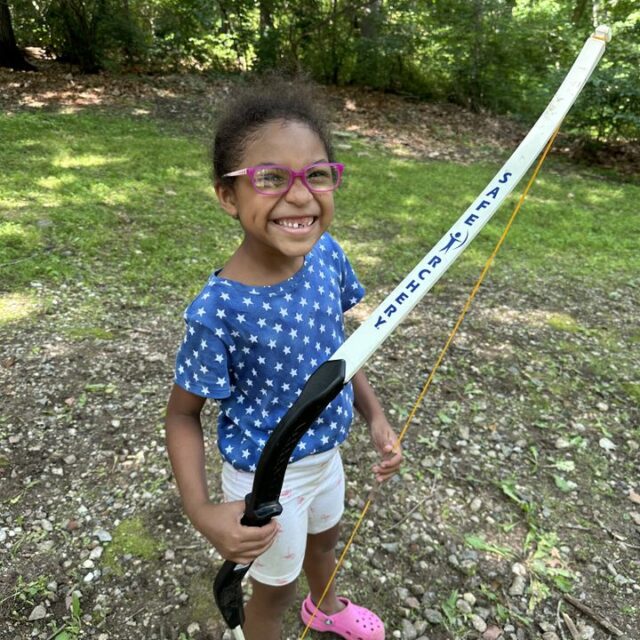 A girl at camp holding a bow and arrow.