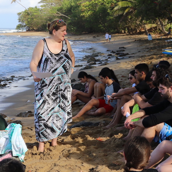 A woman is standing on the beach with a group of people, enjoying the beautiful scenery.