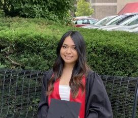 A woman in a graduation gown sitting on a bench.