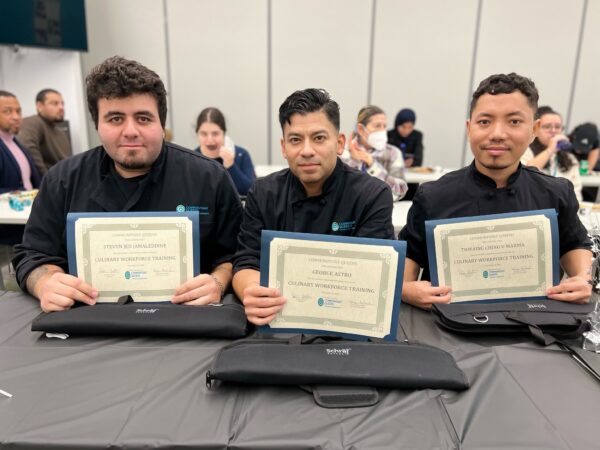Three chefs holding certificates in front of a table after completing their vocational training programs, ready to start their new careers.