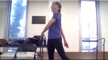 A woman in a purple shirt is standing in a room while following on demand exercise videos.