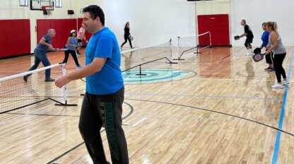 A group of people participating in a commonpoint challenge by playing badminton in a gym.