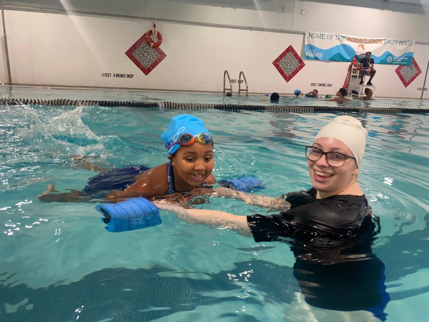 A young girl in a swimming pool with an aquatics teacher.