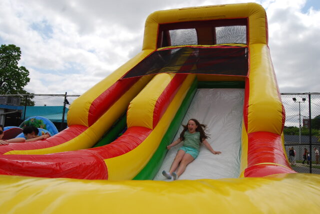 Young girl sliding down a large, colorful inflatable slide at the Kick-Off Carnival in Bay Terrace.