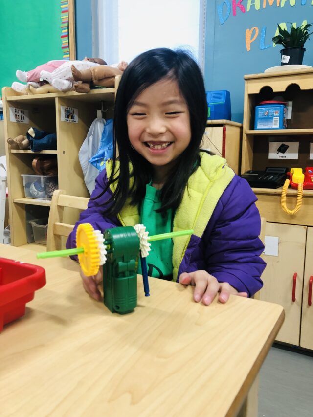 A smiling child with a craft project at a classroom table during holiday programming.